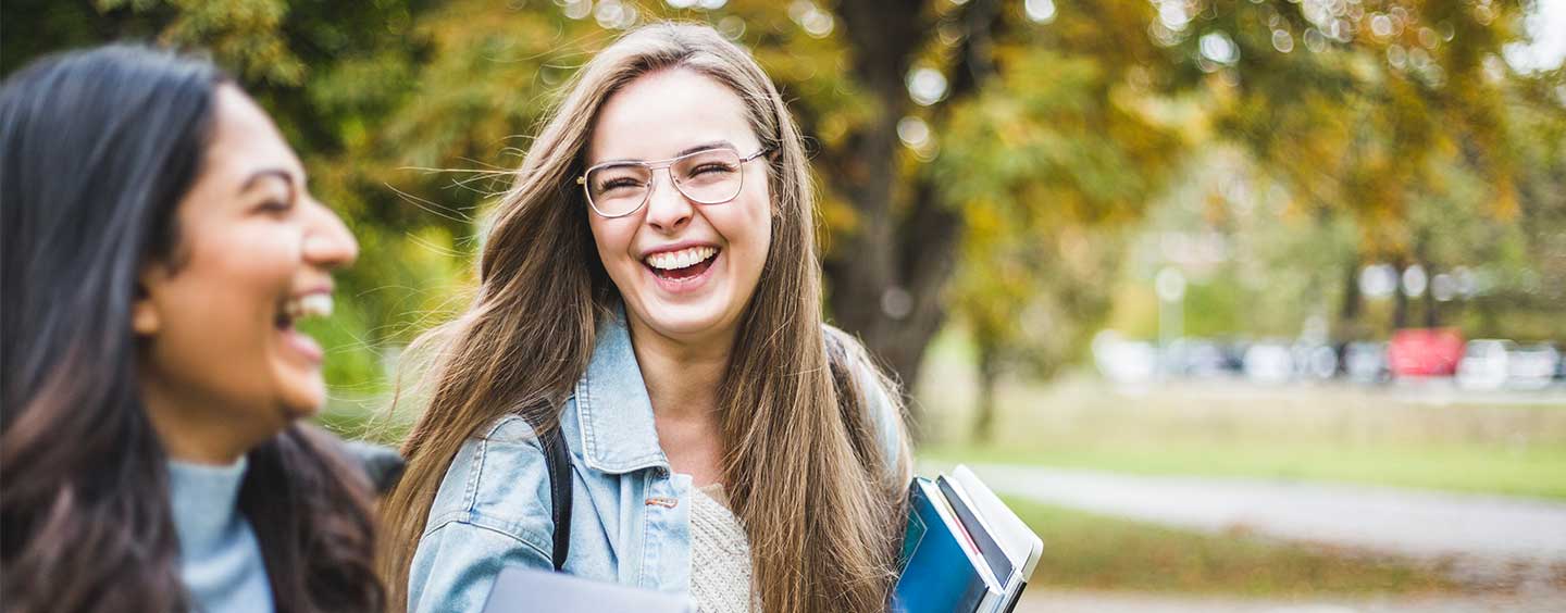 Two women laughing and walking with books